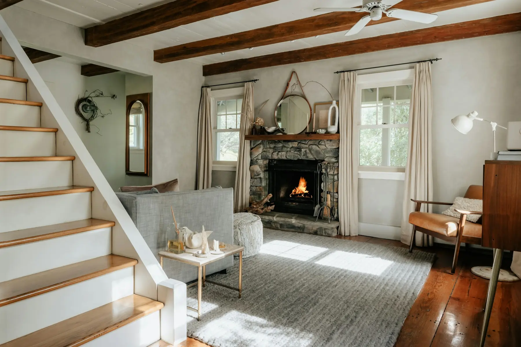 A warm living room with a lit stone fireplace and a staircase