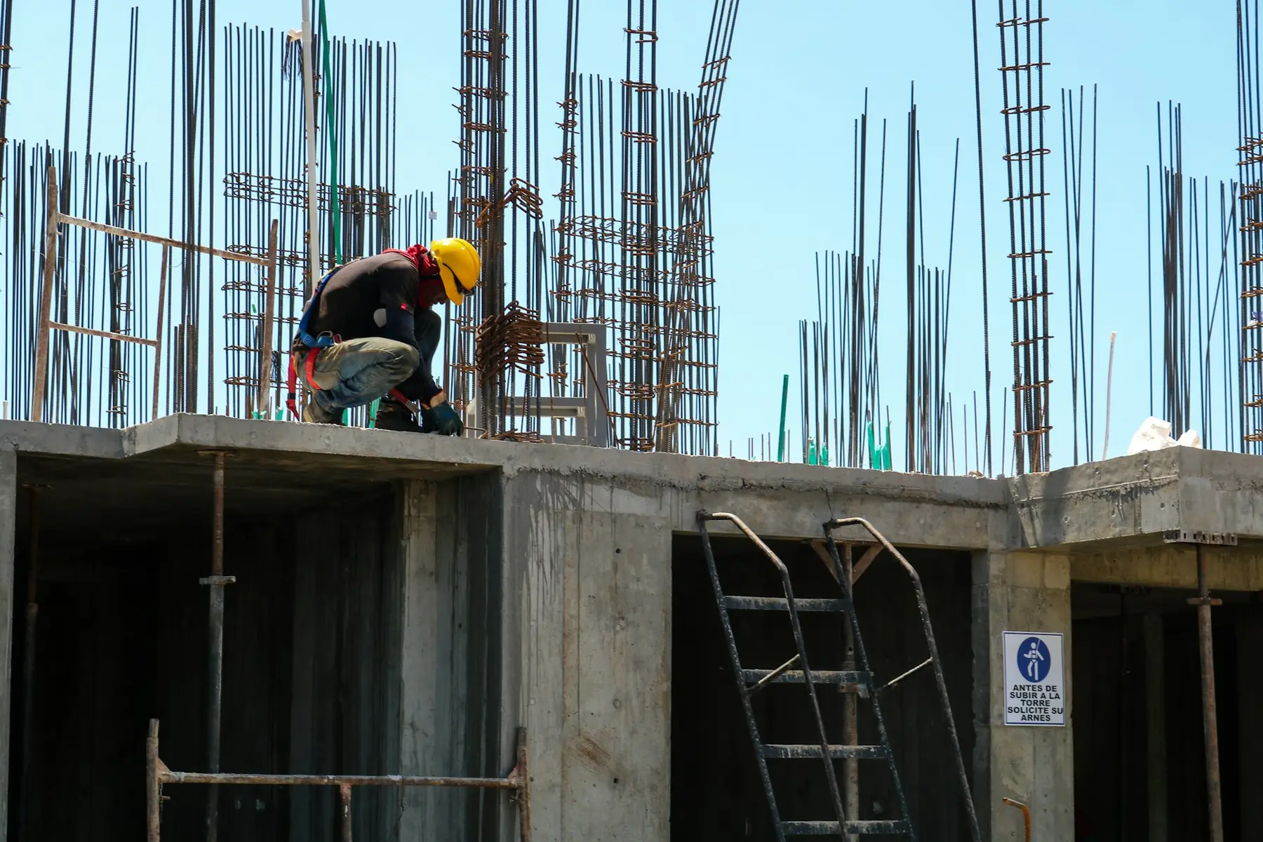 A builder in a hard hat tying rebar on top of a concrete frame