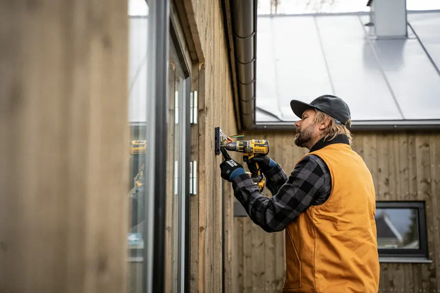 An electrician drilling a fixing into a timber wall
