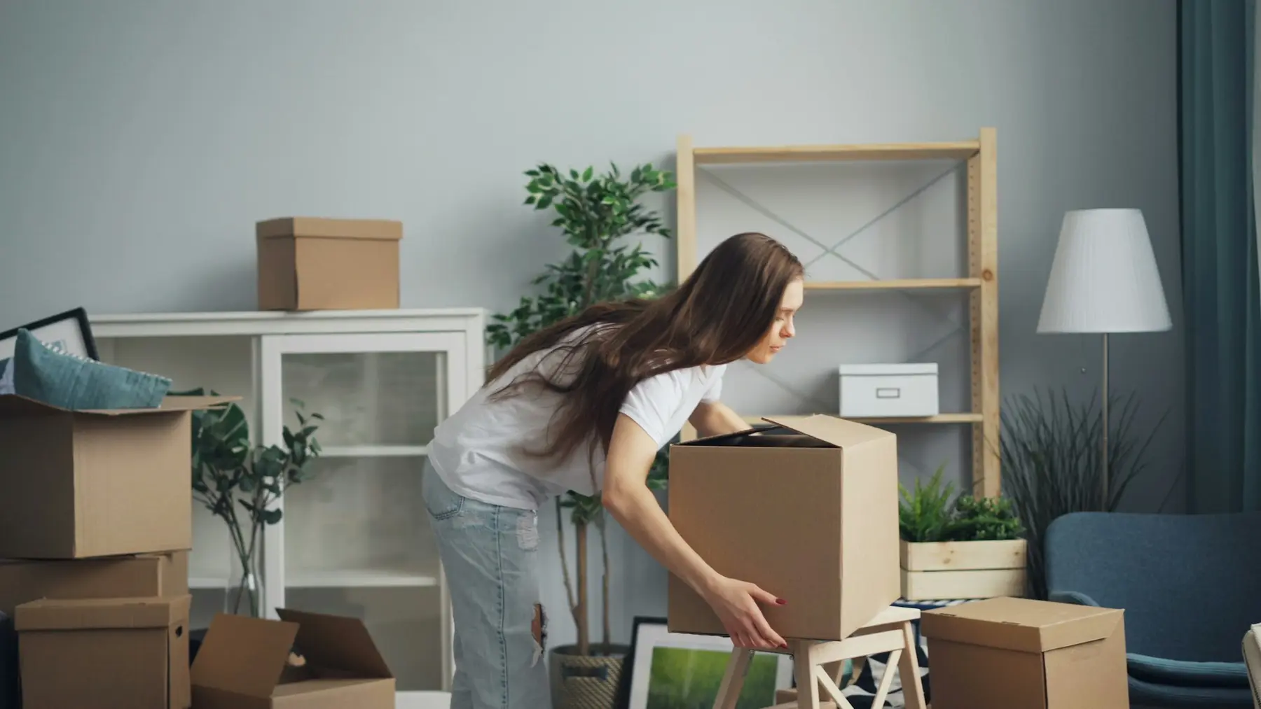 A woman packing a cardboard box in a living room