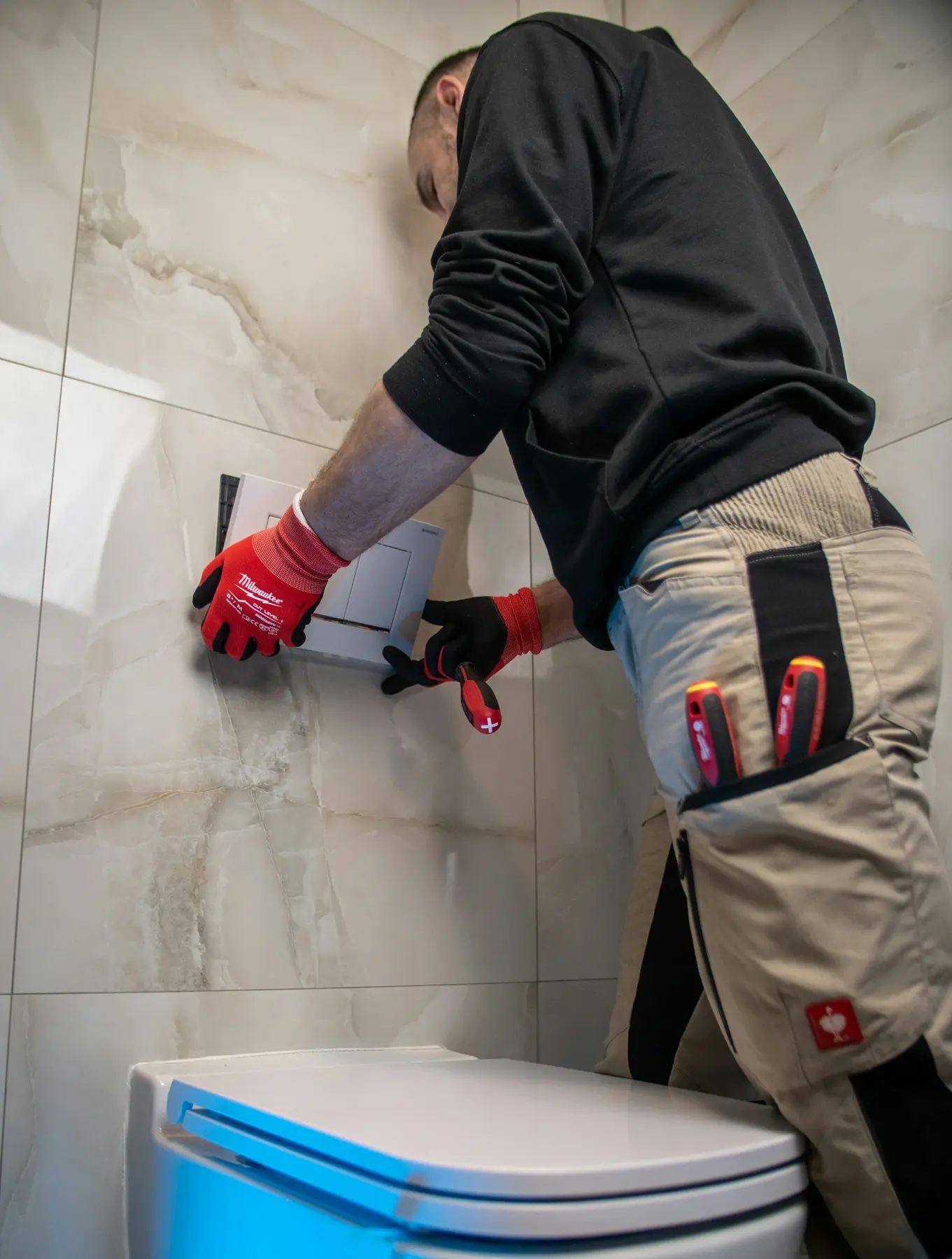 A plumber fitting a wall-hung toilet in a marble-tiled bathroom