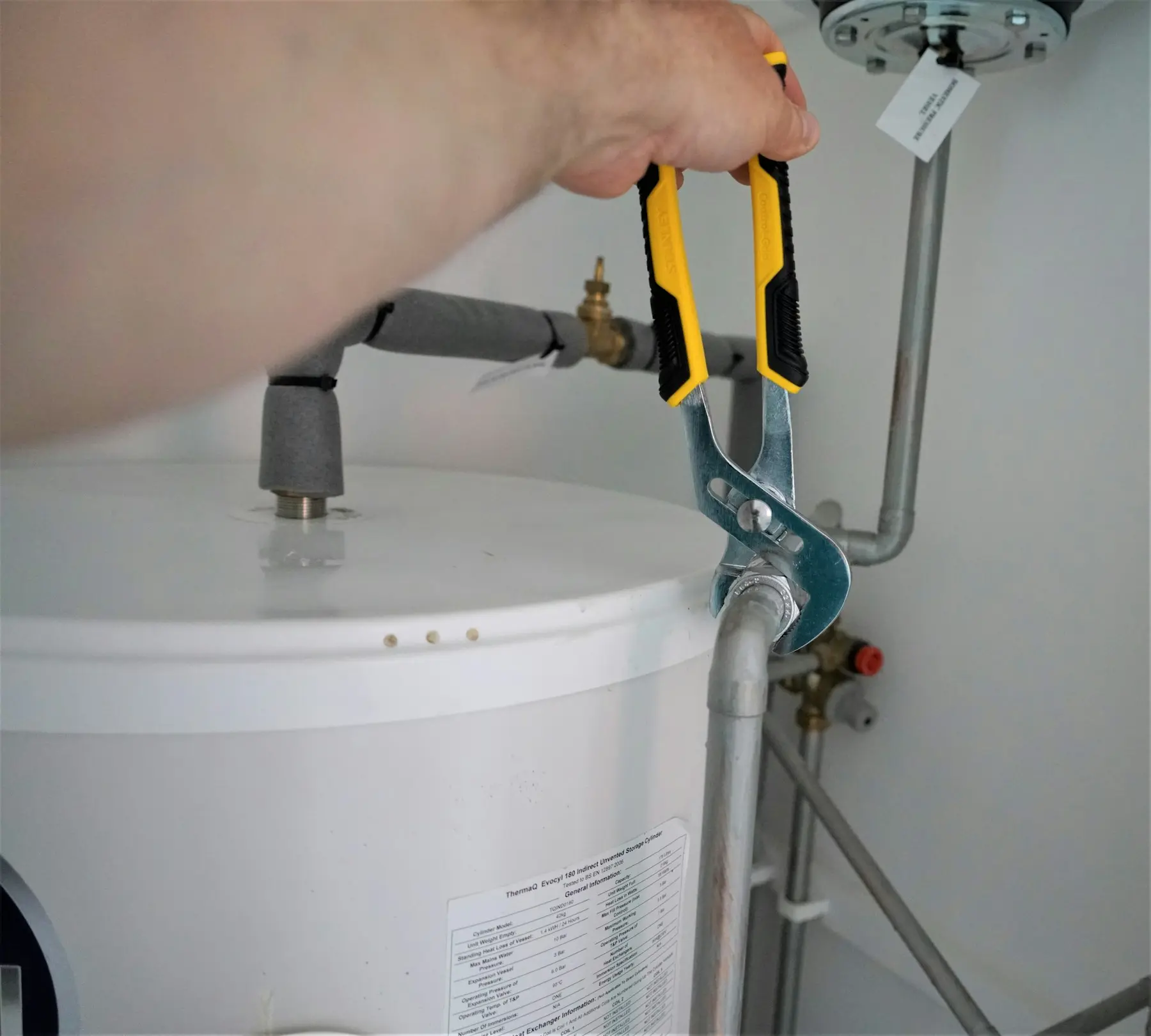 A plumber tightening a fitting on a hot water cylinder