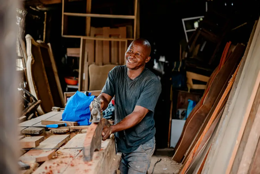 A joiner smiling as he planes timber in the workshop