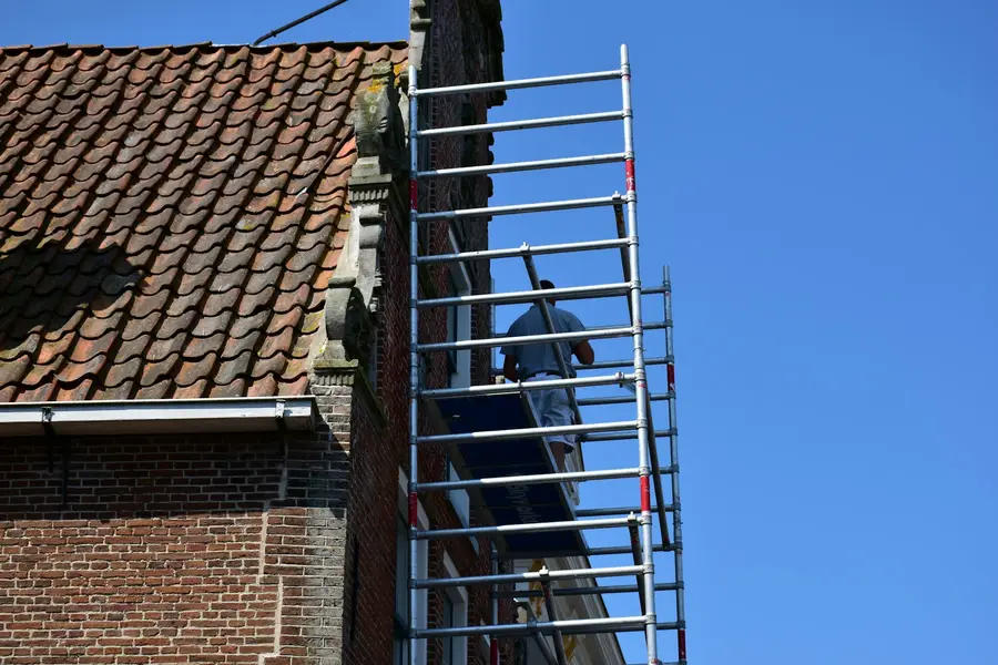 Scaffolding up against a clay-tiled roof on a brick house