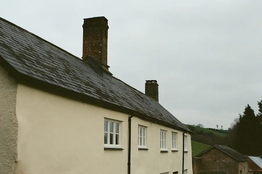 A cream cottage with a dark slate roof and chimneys
