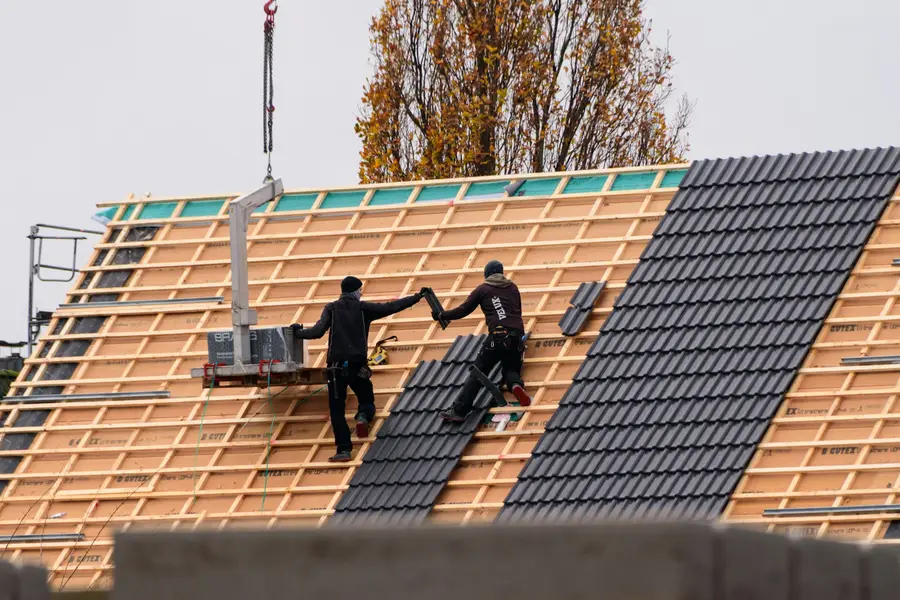 Two roofers laying tiles on a new roof with a crane lifting materials