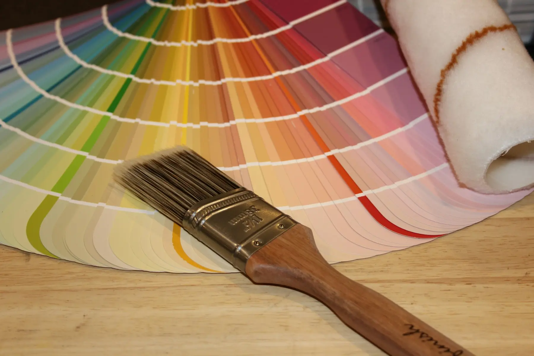 A paintbrush and roller on a fan of colour swatches